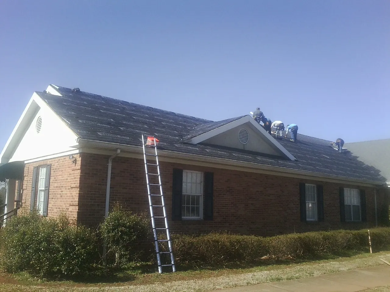 Crew tearing shingles off a brick ranch roof with a ladder set — Emergency Roof Repair work by our crew in Framingham