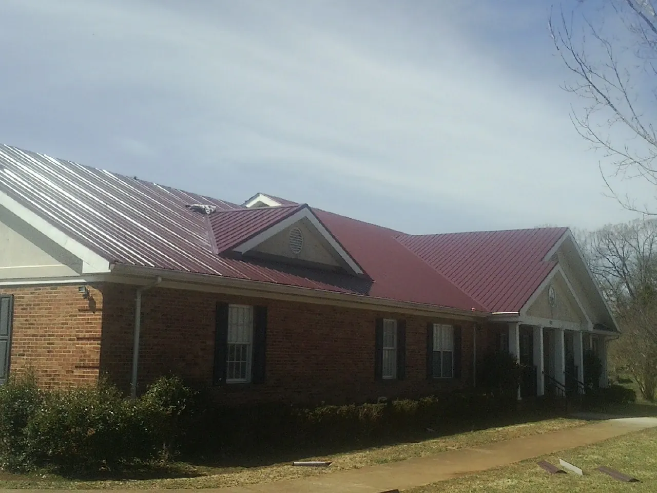 Red metal roof with gabled entries on a long brick building, from a Hail Damage Roof Repair job in Framingham