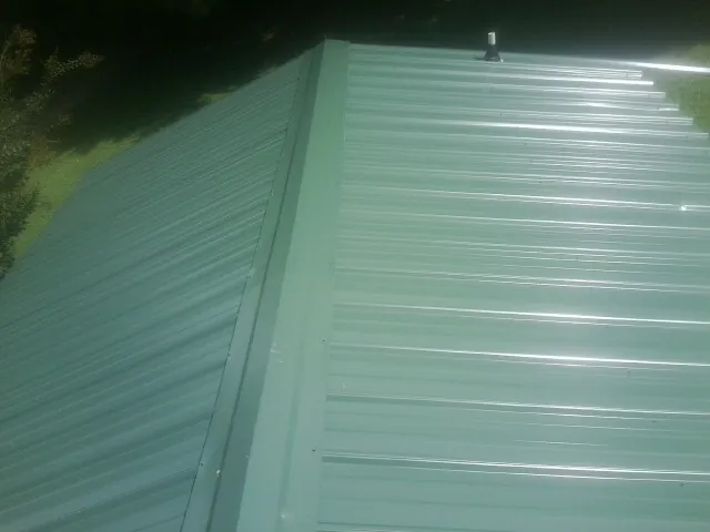 New green metal panels meeting at the ridge of a roof — Flat Roof Repair work by our crew in Framingham
