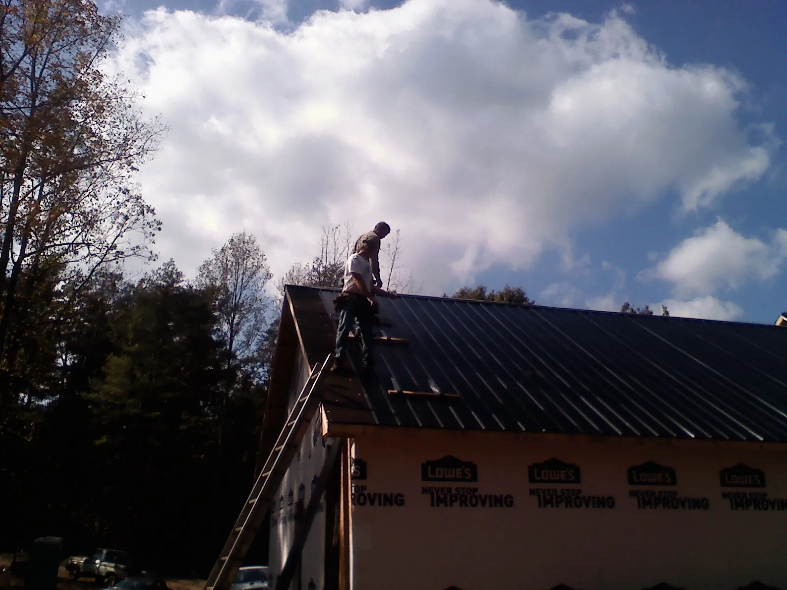 Roofer fastening dark metal panels high against a cloudy sky, from a Roof Inspection job in Framingham