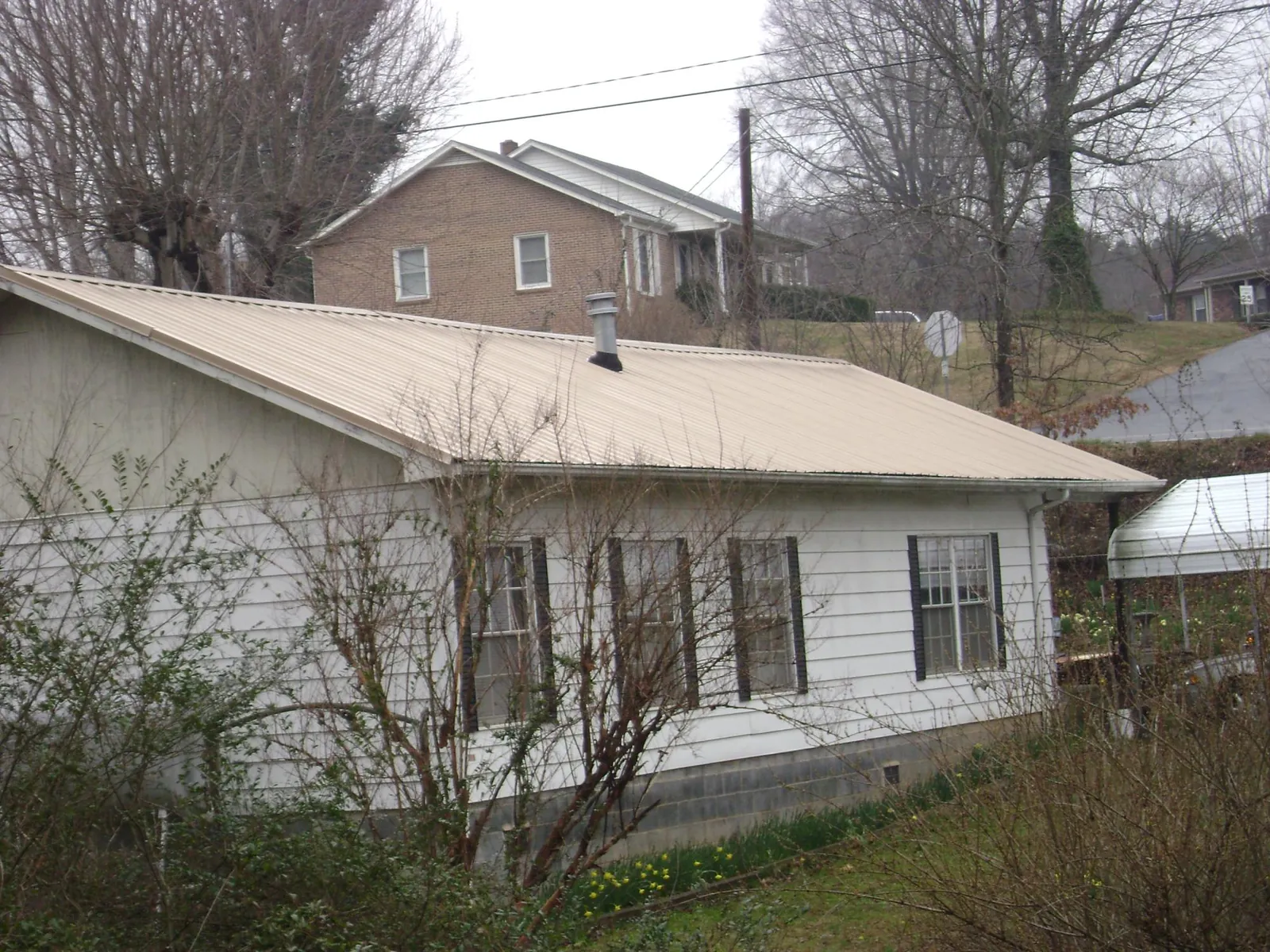 Tan metal roof on a white sided house set into a hillside — Commercial Roofing by Roofing Brothers in Framingham